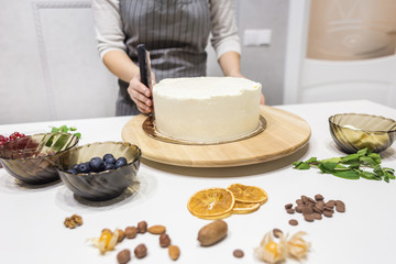 Confectioner smooths white cream on a biscuit cake with a cooking spatula. The concept of homemade pastry, cooking cakes.