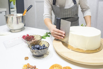 Confectioner smooths white cream on a biscuit cake with a cooking spatula. The concept of homemade pastry, cooking cakes.