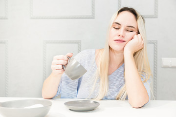 Obraz na płótnie Canvas Young pretty woman falls asleep at breakfast in the kitchen.