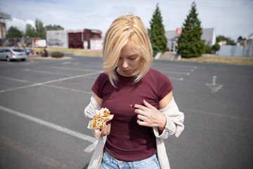 Young beautiful girl eating hot dog in the parking lot. Soiled clothes because of inaccuracy.