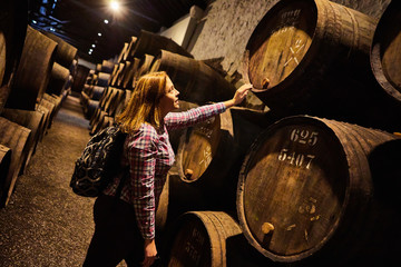 Young woman tourist  walk in old aged traditional wooden barrels with wine in a vault lined up in...