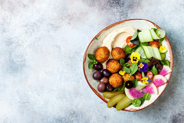 Middle eastern lunch Buddha bowl with hummus, falafel, tomato and greens salad, olives, pickles and...