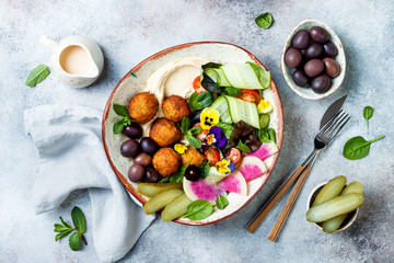 Middle eastern lunch Buddha bowl with hummus, falafel, tomato and greens salad, olives, pickles and edible flowers