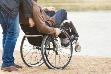 Obraz premium Young man in wheelchair with his assistant on a stroll through the park.