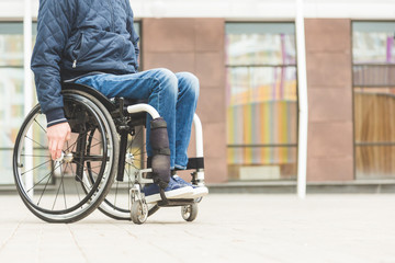 Young man in a wheelchair against the backdrop of a modern high-rise building.