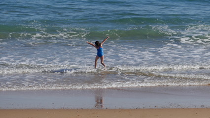 Rear view of a young girl in blue swimsuit. It bathes with much fun in the sea and jumps over the waves.