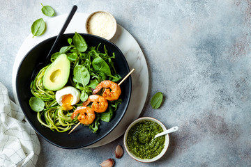 Buddha bowl with soft boiled egg, avocado, greens, zucchini noodles, grilled shrimps and pesto sauce. Vegetarian vegetable low carb lunch bowl.