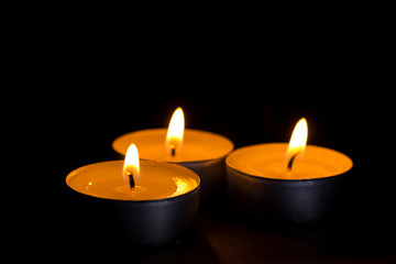 three small candles lit in the dark closeup