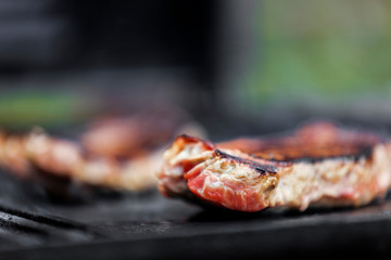 Steak cooking on searing hot outdoor barbecue.