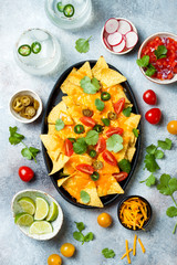 Yellow corn nachos chips with melted cheese sauce, jalapeno, cilantro leaves, tomato salsa and spicy iced margarita cocktail