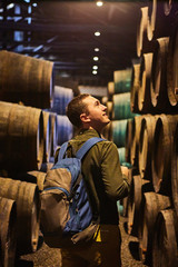 Young man tourist  walk in old aged traditional wooden barrels with wine in a vault lined up in cool and dark cellar in Italy, Porto, Portugal, France