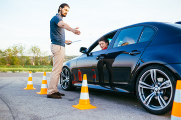 Driving school or test. Beautiful young woman with instructor learning how to drive and park car between cones.