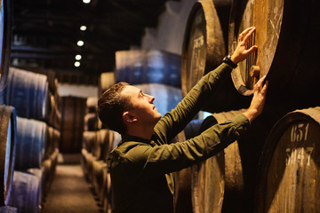 Professional winemaker male  in old aged traditional wooden barrels with wine in a vault lined up...