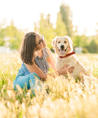 Pretty brunette woman playing with a dog white golden retriever on the grass in park. Woman with her dog on green meadow, puppy training