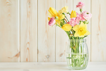 bouquet of spring flowers: tulips, carnations, ranunculi and daffodils in a vase on a table on a white wooden background