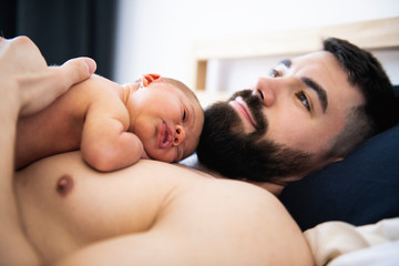 father lay on bed with his newborn baby daughter