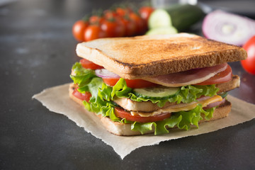Sandwich with bacon, tomato, onion, salad on black. Close up.