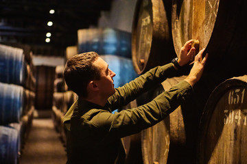 Professional winemaker male  in old aged traditional wooden barrels with wine in a vault lined up...