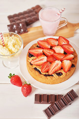 Strawberry cake and chocolate bars on a white wooden background.