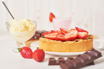 Strawberry cake and chocolate bars on a white wooden background.