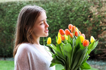 Beautiful smiling happy tween girl holding big bouquet of bright yellow and orange tulips talking...