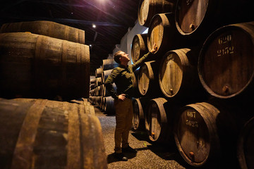 Professional winemaker male  in old aged traditional wooden barrels with wine in a vault lined up...