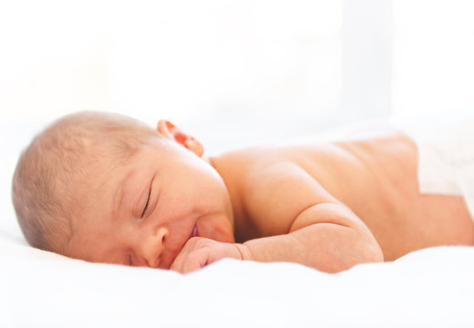 A newborn baby laying down sleeping on a soft white background. Use the photo to represent life, parenting or childhood.