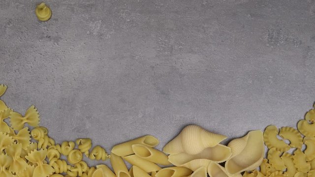 Different dried pasta moving on grey kitchen table. 4K Stop motion animation.