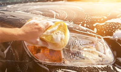Man washing a soapy  car with a yellow sponge.