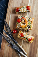 Delicious sandwich with grilled shrimp and cherry tomatoes on a wooden board decorated with pheasant bird feathers.