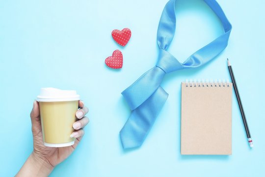Creative flat lay of Father's Day concept. Necktie, notebook and woman hand holding coffee cup on pastel colour background