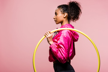 side view of beautiful african american sportswoman posing with hula hoop isolated on pink with copy space