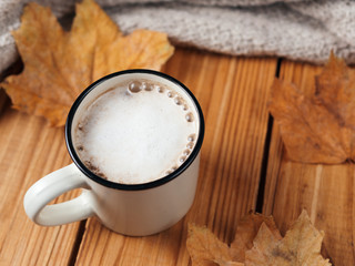 Autumn cappuccino with cinnamon on wooden background. Hot coffee with dry leaves and scarf