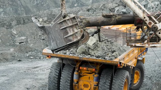 Excavator fills dump truck. Bucket excavator closeup loads stones into body of dump truck on mining or construction of something