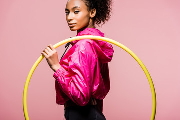 beautiful african american sportswoman holding hula hoop and looking at camera isolated on pink - obrazy, fototapety, plakaty