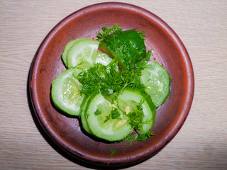 Freshly cut green cucumber with herbs in a clay plate.