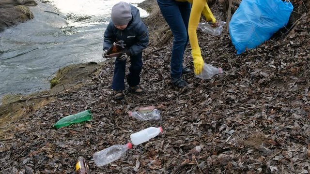 Woman volunteer with her child cleaning up the trash by the river. Ecology and environment concept