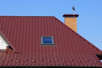 part of the house with red tiles on the roof with a window and a brick pipe against the sky