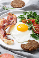 Hearty high protein english style breakfast with egg, fried bacon and arugula on the plate. Top view, vertical orientation