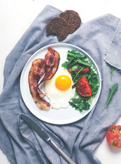 Hearty high protein english style breakfast with egg, fried bacon and arugula on the plate. Top view, vertical orientation