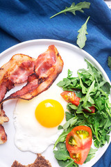Hearty high protein english style breakfast with egg, fried bacon and arugula on the plate. Top view, horizontal orientation