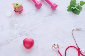 flat lay of good healthy concept, pink dumbbell with red heart and stethoscope and green apple on white marble background