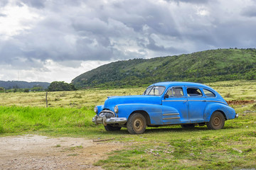 Fototapeta premium HAVANA, CUBA - JANUARY 04, 2018: A retro classic American car parked against the backdrop of mountains and overcast sky in Cuba