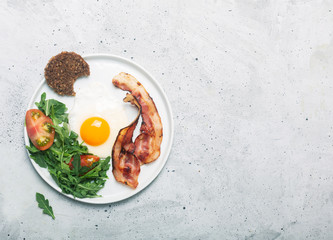 Hearty high protein english style breakfast with egg, fried bacon and arugula on the plate. Top view, horizontal orientation