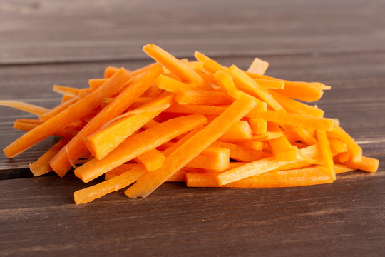 Lot of pieces of fresh orange carrot cut into thin noodles on brown wood