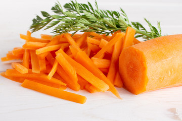 One half lot of pieces of fresh orange carrot cut into thin noodles with greens on white wood