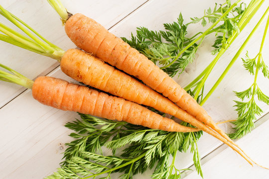 Group of three whole fresh orange carrot with greens flatlay on white wood