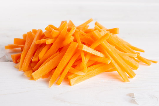 Lot of pieces of fresh orange carrot cut into thin noodles on white wood
