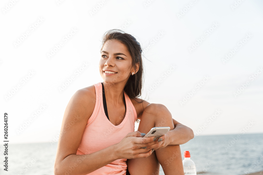 Sticker Attractive young fitness woman using mobile phone