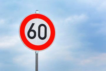 Red round 60km/h speed limit sign on highway in front of blue sky
